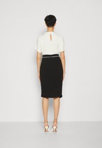 Černá tužková sukně s bílým páskem, kombinovaná s bílým topem s detaily ve tvaru klíčové díry na zádech. Hladký materiál, přiléhavý střih.