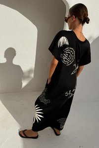 Czarna, oversize sukienka t-shirtowa z białymi nadrukami graficznymi liści palmowych i tekstem, o luźnym kroju i krótkich rękawach.