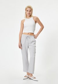 Lichtgrijze, loszittende broek met een elastische tailleband met trekkoord, gecombineerd met een nauwsluitend wit geribbeld tanktop. Platte witte schoenen zichtbaar.