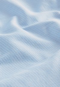 Tessuto azzurro chiaro con un motivo strutturato di piccoli crocini intrecciati che creano dolci pieghe e ombre.