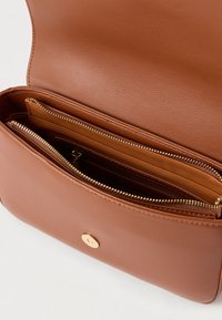 Smeđa kožna torba preko tijela s glatkom teksturom, s više pretinaca na patentni zatvarač i detaljem od zlata boje na kopči.