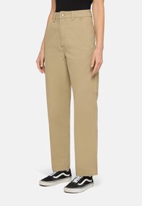 Beige hooggetailleerde broek met rechte pijpen, gemaakt van een stevige stof, met zijzakken en een knoopsluiting. Gecombineerd met zwarte sneakers.