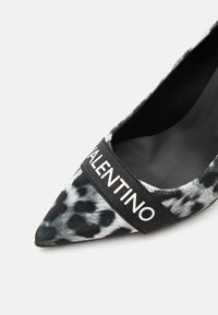 Chaussure femme à bout pointu avec imprimé léopard noir et blanc et bride noire portant l'inscription « VALENTINO » sur le dessus.