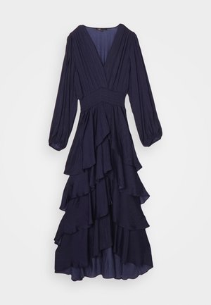 Mornarska haljina s dugim rukavima i dubokim V-izrezom, s nabranim tijelom i slojevitim volanima na rubu. Napravljena od lagane tkanine s mekanom teksturom.