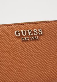 Sac à main en faux cuir texturé marron avec un logo argenté "GUESS EST 1981" mis en avant sur le devant.