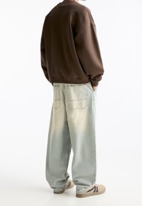 Felpa oversize marrone e jeans a gamba larga blu chiaro. La felpa presenta un col rotondo e i jeans hanno un lavaggio sbiadito con tasche posteriori.
