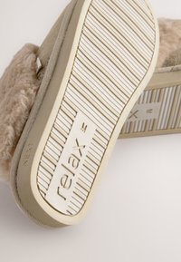 Chausson beige avec dessus duveteux, semelle en caoutchouc à motif texturé et marquage en relief "relax" près du talon.
