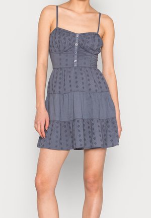 Vestido gris con tirantes finos, con cuerpo ajustado, cierre de botones y falda de capas con volantes que presenta patrones de ojal y tela texturizada.