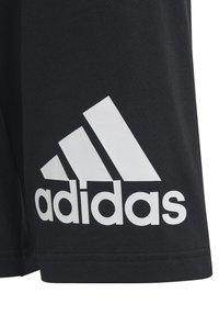 Pantalones cortos negros de tejido suave con un gran logo blanco de Adidas y tres franjas diagonales distintivas. Diseño simple y funcional.