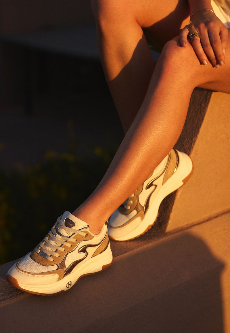 Zapatillas con una base de cuero blanco, acentos de ante gris y detalles metálicos. Suelas de goma gruesa y costuras en contraste.
