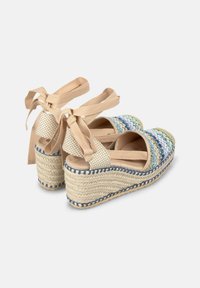 Sandalias de cuña con suela de yute trenzado, parte superior de tejido multicolor y lazos de tela beige en el tobillo. Presenta una puntera redonda y acentos texturizados.