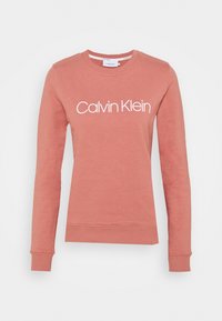 Sudadera Calvin Klein en coral con mangas largas, cuello redondo y texto del logo en blanco en la parte delantera. Textura suave, puños y dobladillo acanalados.