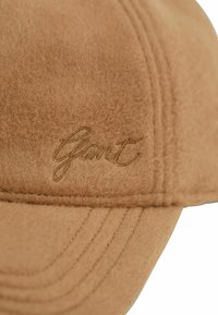 Tan gekleurde pet met een geborduurd "Gant" logo. Gladde textuur met stikdetails en een iets gebogen rand.