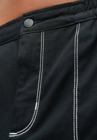 Μαύρα υφασμάτινα σορτς με λευκά ραφές σε αντίθεση και μαύρο κουμπί στο κλείσιμο. Το υλικό φαίνεται ανθεκτικό και με υφή.