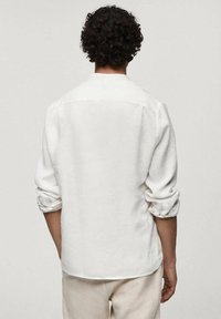 Chemise en lin blanche à manches longues, retroussées aux poignets, avec un col classique et un dos droit. Texture légère.