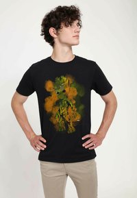 Zwarte t-shirt met een kleurrafische afbeelding van Groot uit Marvel's "Guardians of the Galaxy," met groene en oranje accenten op een zwarte achtergrond.