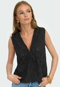 Zwarte mouwloze blouse van gestructureerde stof, met een diepe V-hals, geborduurde bloemenpatronen en een strik in de taille.