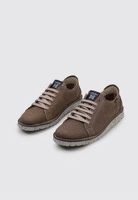 Zapatillas de cuero marrón con cordones gris claro, que presentan una suela texturizada con manchas negras y una etiqueta azul en la lengua. Diseño de perfil bajo.