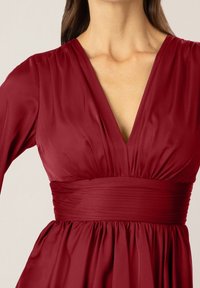 Röd satin klänning med djup V-ringning, rynkad midja och långa ärmar; slät textur med en flödande kjol.
