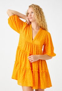 Orangenes Kleid aus strukturiertem Stoff; hat einen tiefen V-Ausschnitt, Puffärmel und einen gestuften Rüschensch skirt.