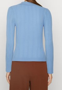 Pull à col bleu clair côtelé, au design ajusté et à manches longues, associé à un pantalon marron taille haute.