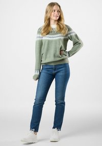 Groene gebreide trui met een ruitpatroon in wit en blauw, relaxed fit, geribde manchetten en zoom, gecombineerd met blauwe jeans en witte sneakers.