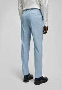 Lichtblauwe op maat gemaakte broeken met een subtiele textuur, riemlussen en een achterzakdetail. Gecombineerd met zwarte schoenen.