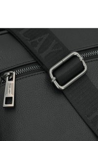 Borsa nera in pelle sintetica con superficie testurizzata, dotata di hardware in metallo per la zip e di una tracolla regolabile con branding in rilievo.