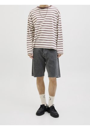 Top de manga larga a rayas en crema y marrón, combinado con shorts de mezclilla negros. Estilizado con calcetines blancos y zapatos negros para un look casual.