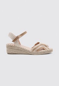 Sandalia de cuña con parte superior de textil trenzado en tono marrón, punta cerrada, diseño de correas cruzadas y suela de yute trenzado. Incluye correa ajustable para el tobillo.