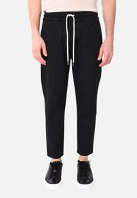 Pantaloni da jogging neri in cotone con vita elastica, cordoncino regolabile, tasche laterali e gambe affusolate. Abbinati a sneakers nere.