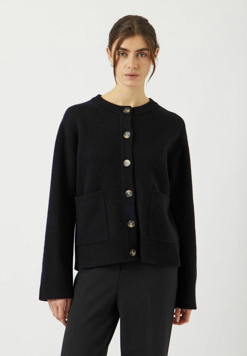 Mörk marinblå cardigan i mjukt stickat material, med rund halsringning, sex stora knappar, två framfickor och långa ärmar.