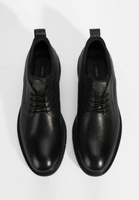 Chaussures en cuir noir avec une surface texturée, un design à lacets et un bout rond. Présentent une boucle à l'arrière et une semelle en caoutchouc lisse.