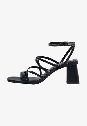 Sandale noire à brides avec talon bloc, bride à boucle à la cheville, et multiples fines brides croisées sur le pied et les orteils, vue de profil.