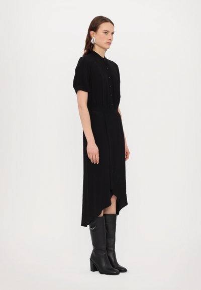 Rochie midi neagră cu închidere prin butoane în față, mâneci scurte și tiv asimetric. Stilizată cu cizme negre până la genunchi și un accesoriu argintiu.