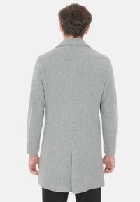 Cappotto grigio in lana visto da dietro. Presenta una vestibilità su misura, colletto a rever e una fessura posteriore singola per la mobilità. Le maniche lunghe sono a taglio dritto.