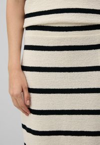 Gewebtes Strickkleid in Creme mit schwarzen horizontalen Streifen. Verfügt über eine strukturierte Oberfläche und ein gefaltetes Kragen-Detail.