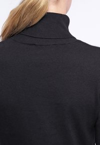 Svart tröja med design av hög polokrage, med ribbat mönster och stickadtyg. Vyn visar baksidan utan synliga logotyper eller mönster.