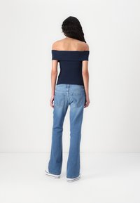 Top blu navy con scollo a spalle scoperte abbinato a jeans chiari a campana. L'outfit presenta un design aderente e una classica texture in denim. Sneakers bianche in basso.