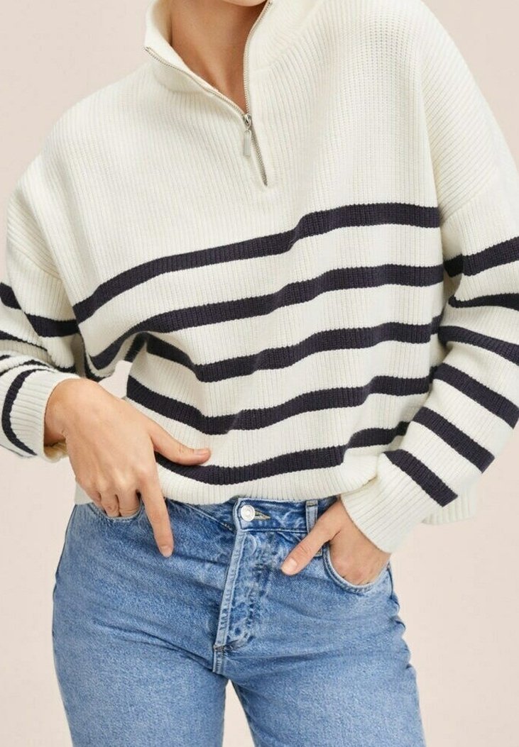Cream striped pullover sweater with a high collar and half zip; features navy horizontal stripes and ribbed texture. Paired with blue denim.