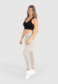 Zwarte sportbeha en beige leggings van rekbaar materiaal, met een hoge taille en naadloos ontwerp, gecombineerd met witte sportschoenen.