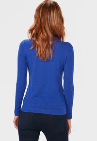 Pull à manches longues bleu en tricot. Présente une silhouette ajustée et un ourlet côtelé. Texture lisse et design minimal.