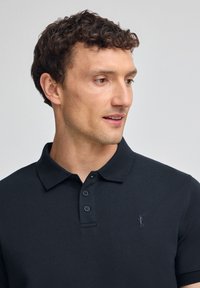 Polo negro hecho de algodón, con un collar clásico, tapeta de tres botones y un logo bordado en el lado izquierdo del pecho.