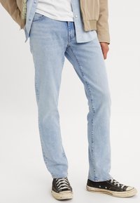 Lyseblå denimjeans med rett passform, med et klassisk fem-lommer design og slitte svarte joggesko med hvite snøringer.