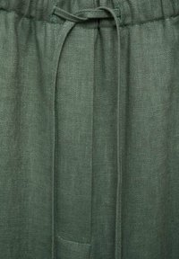 Gros plan sur un pantalon en lin vert olive avec un cordon noué en nœud à la ceinture élastique.