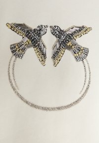 Silverfärgad brosch med två fåglar prydda med svarta och klara rhinestones, med en böjd silverkedja nedan. Texturerad och detaljerad design.