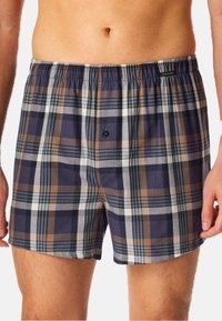 Boxers en tartan en coton, de couleur marine, marron et blanche. Dotés d'une ceinture élastique et d'une fermeture à bouton à l'avant.