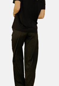 T-shirt noir associé à un pantalon vert foncé brillant avec une texture subtile et un design fluide. L'ensemble est décontracté et au style relax.