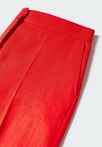 Jupe rouge taille haute avec une ceinture et un détail subtil de pli à l'avant sur fond blanc.