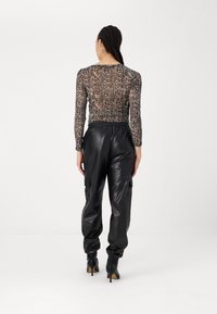 Langmouw, semi-transparante top met slangenprint, gecombineerd met zwarte nep-lederen cargobroek en enkelsandalen. Achteraanzicht.